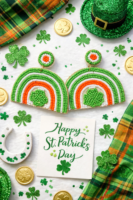 Flat lay of green white and orange beaded rainbow shamrock St. Patrick’s Day statement earrings surrounded by shamrock decor