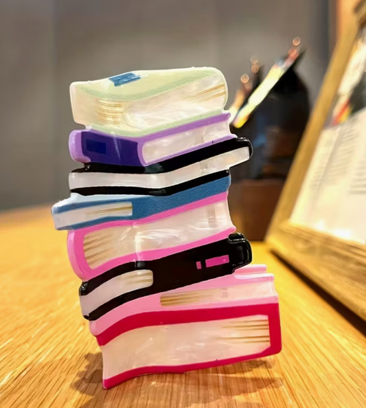 Multicolor stacked-books acrylic hair clip standing upright on a wooden surface.