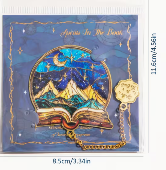 Metal book lover bookmark with mountain and starry sky design displayed on decorative blue backing card.