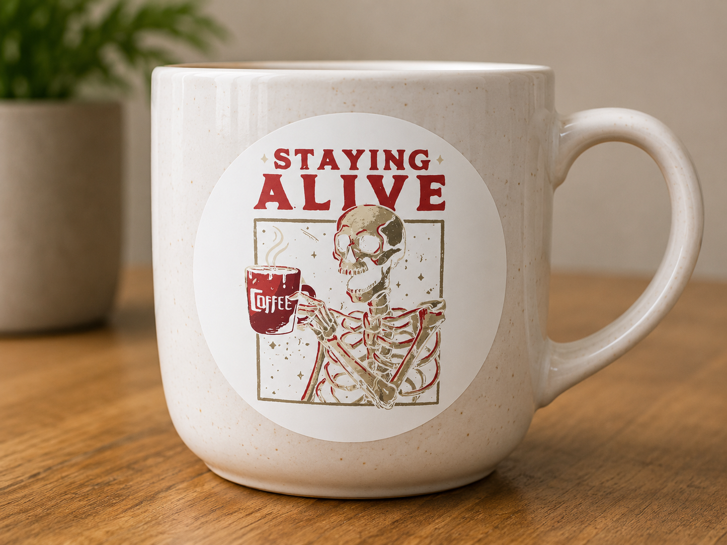 Round Staying Alive coffee vinyl sticker featuring a skeleton holding a coffee mug displayed on a ceramic mug.