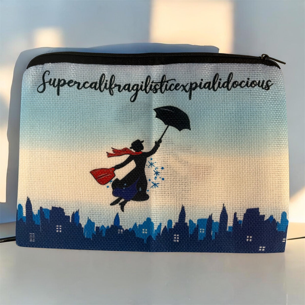 Supercalifragilisticexpialidocious zipper pouch featuring a magical nanny with umbrella and handbag flying above a blue London skyline