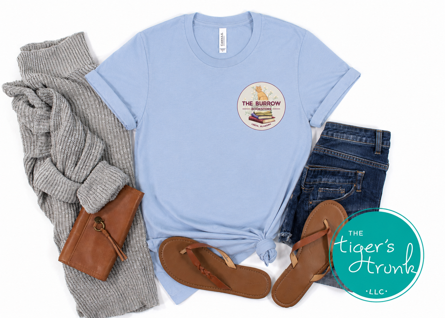Light blue bookstore graphic T-shirt styled in a flat lay with jeans, sandals, and cardigan.