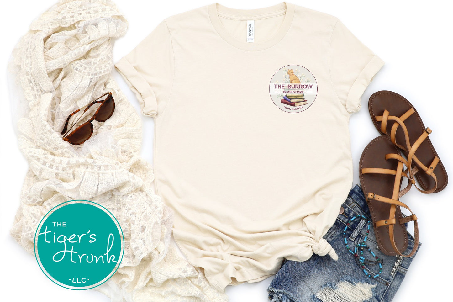 Natural bookstore T-shirt styled in a flat lay with jeans, sandals, and accessories.