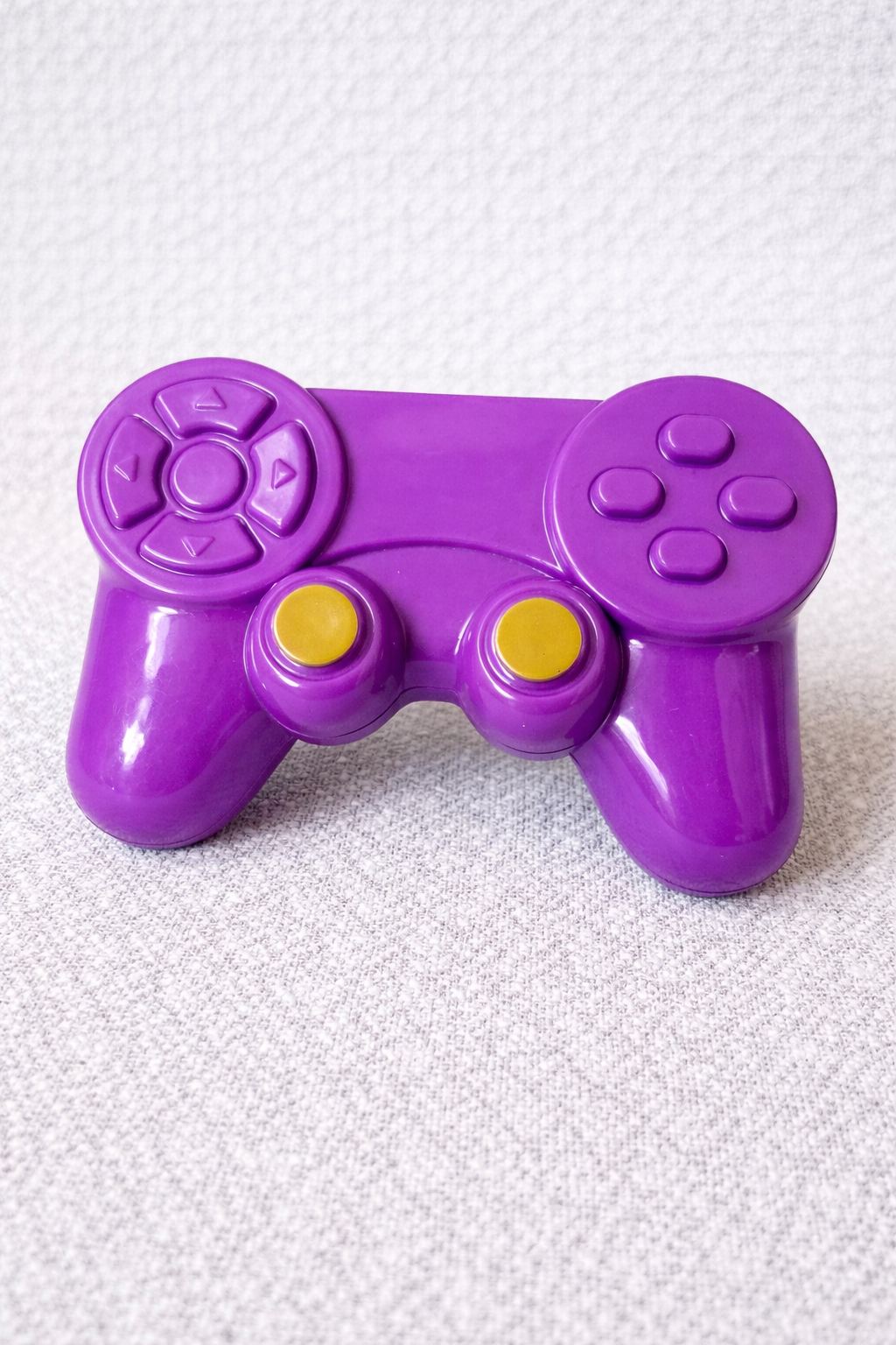 Purple toy controller with yellow buttons on a textured white background