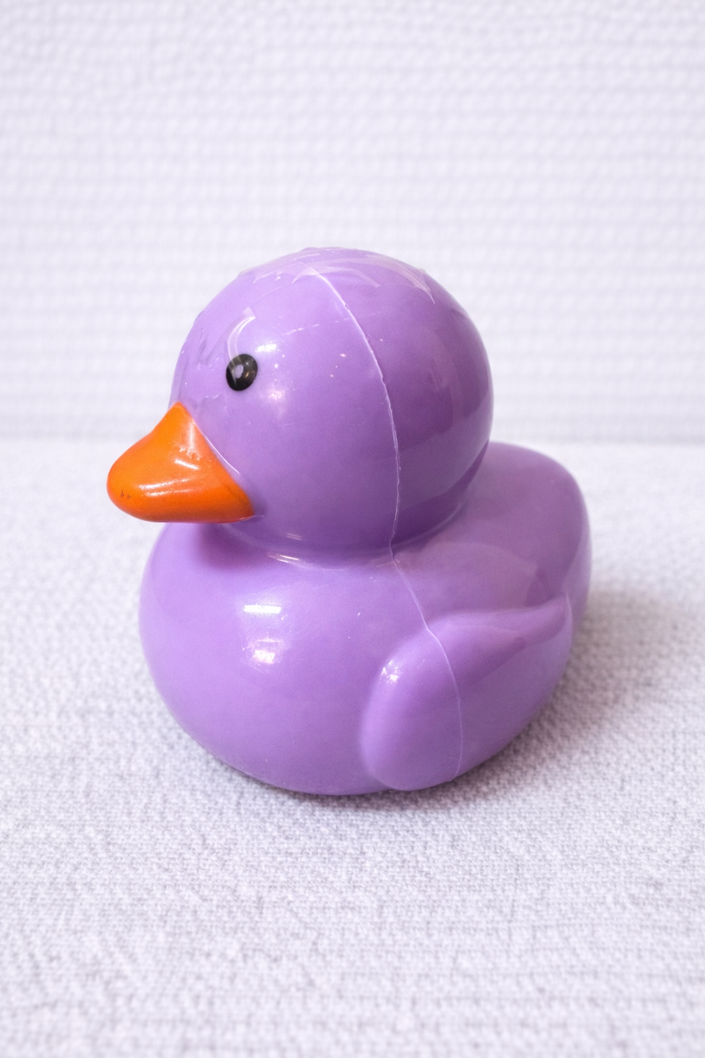 Purple rubber duck with an orange beak on a white background