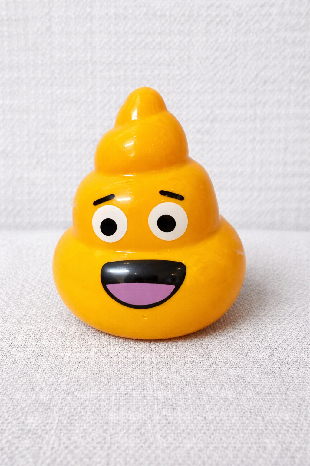 Yellow emoji toy shaped like a poopy face on a white background