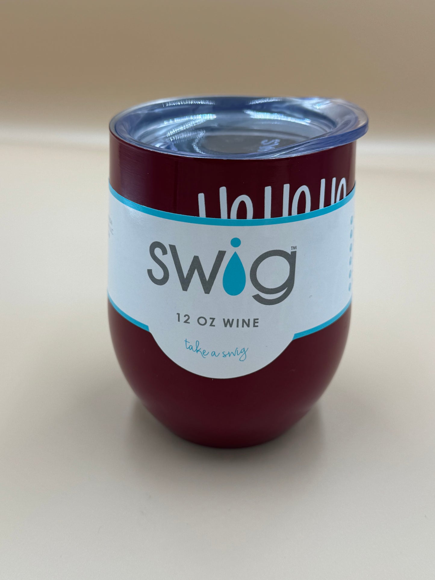 Maroon wine tumbler with blue lid and 'Swig' label on a beige background