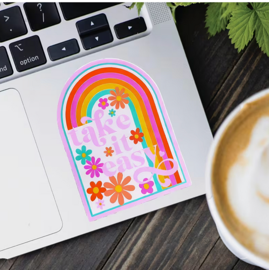 Colorful Take It Easy retro rainbow vinyl sticker with bright pink, orange, yellow, and turquoise arches and cheerful flowers displayed on a silver laptop.