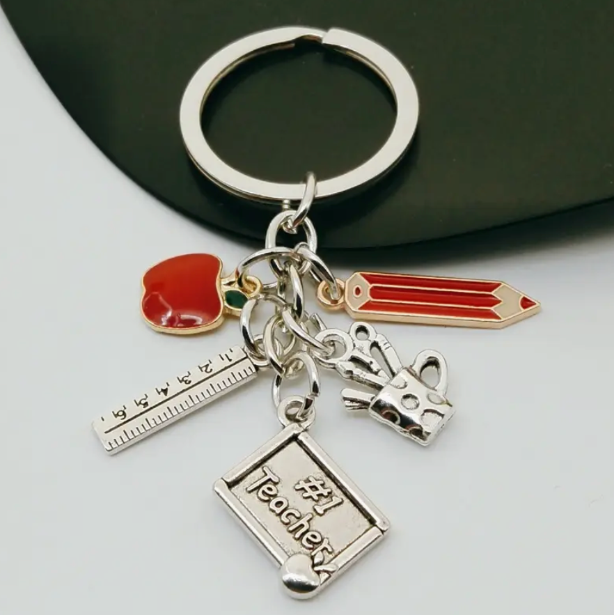 Metal keychain featuring a red pencil and apple, silver ruler, mug with writing utensils, and a plaque that says #1 Teacher—a thoughtful gift for educators.