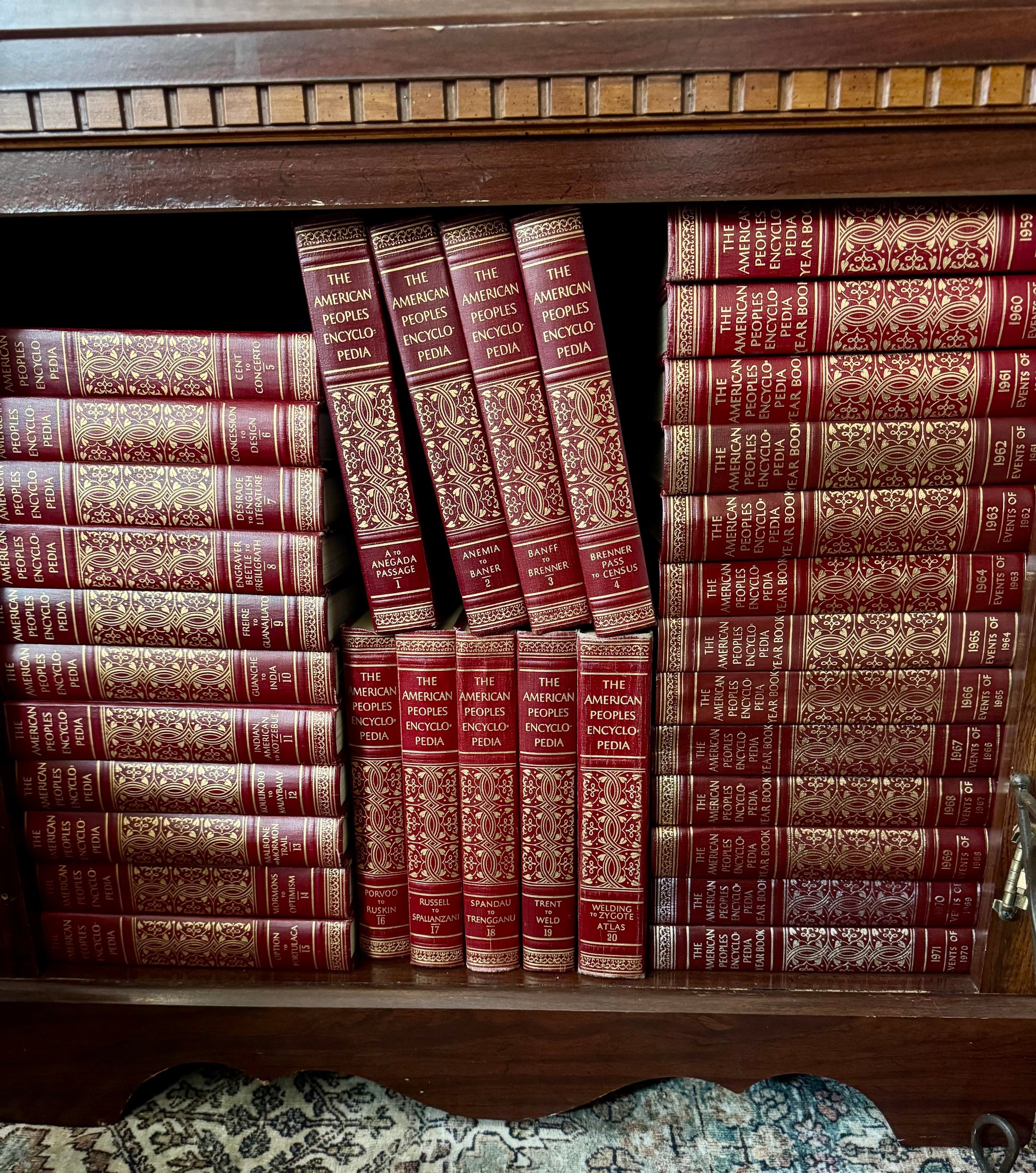 Stack of wrapped presents with a card on a wooden floor next to a bookshelf.