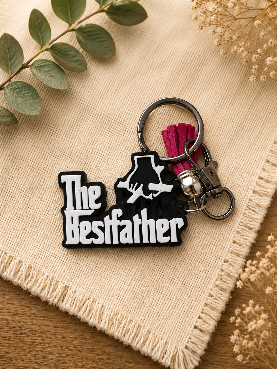 Black and white The Bestfather keychain with pink tassel and lobster clasp attachment on cream fabric background