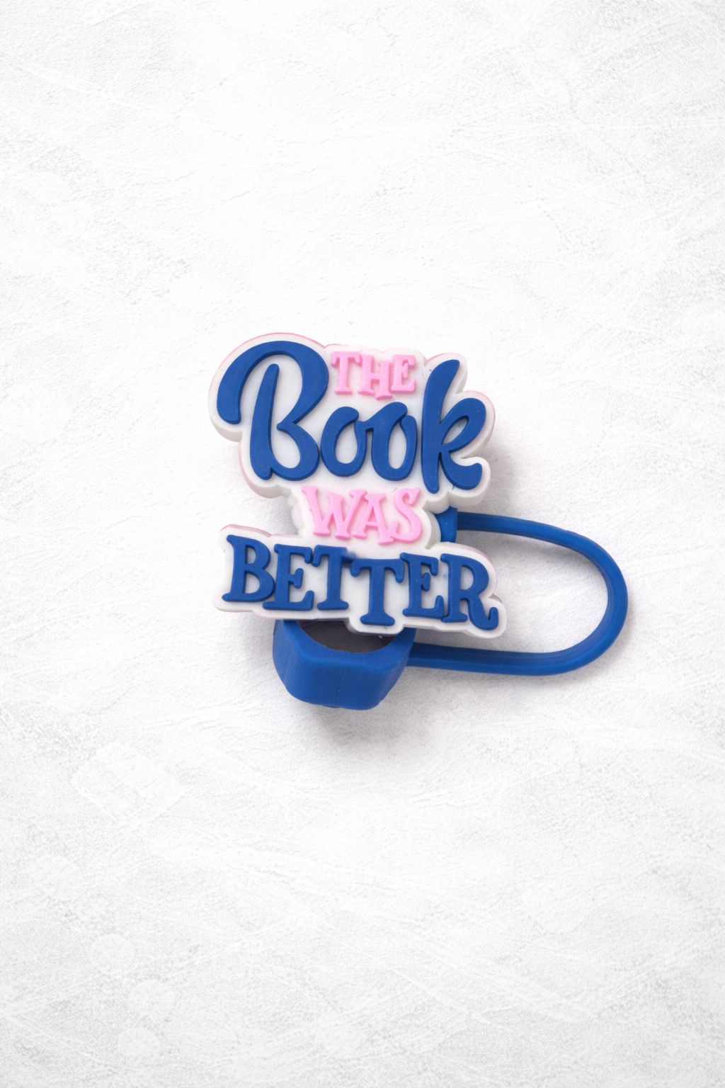 Blue and pink silicone straw topper reading The Book Was Better with flexible loop attachment for reusable tumbler straw.