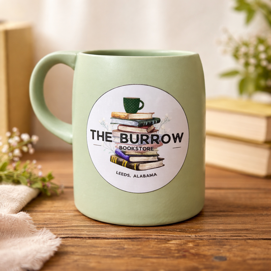 Light green mug with 'The Burrow Bookstore' logo on a wooden surface.