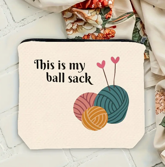 Canvas pouch with yarn ball design and text 'This is my ball sack' on a textured surface.