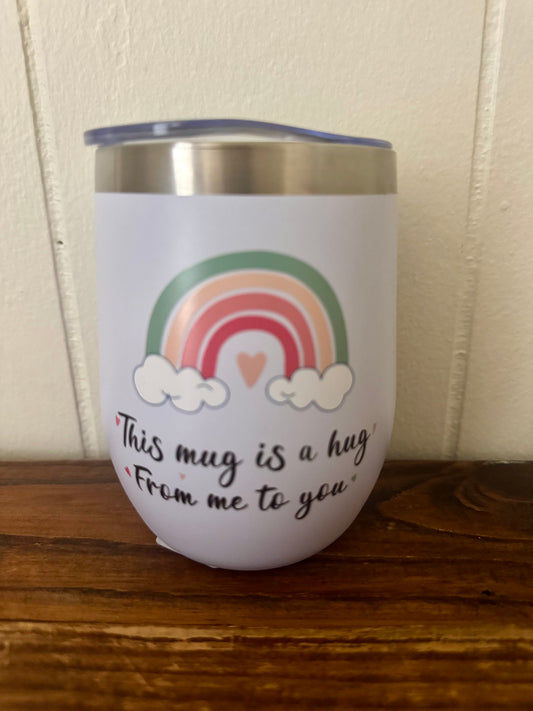 White tumbler with rainbow design and text on a wooden surface