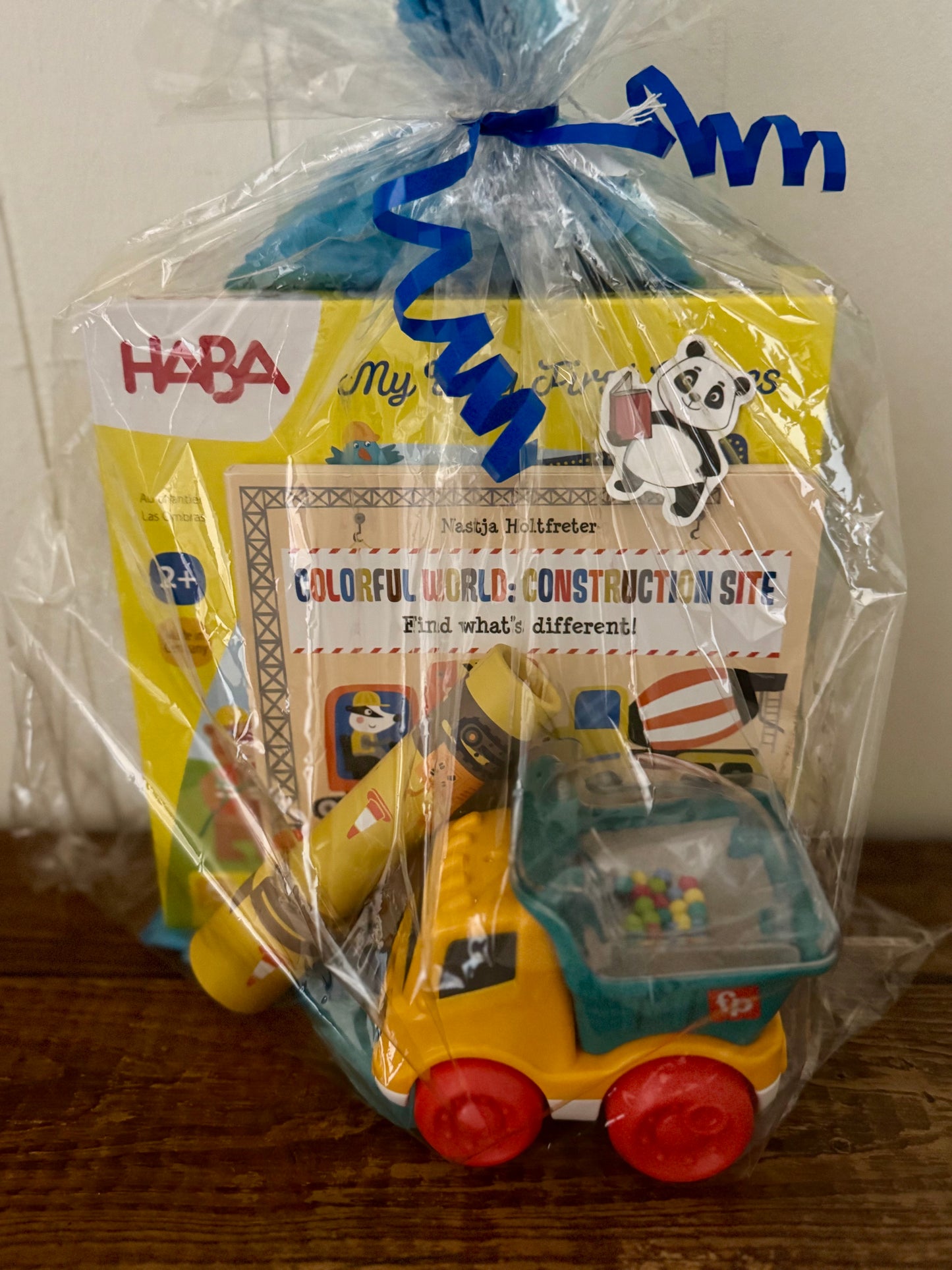 Toy truck in a clear plastic bag with HABA branding on a wooden surface.