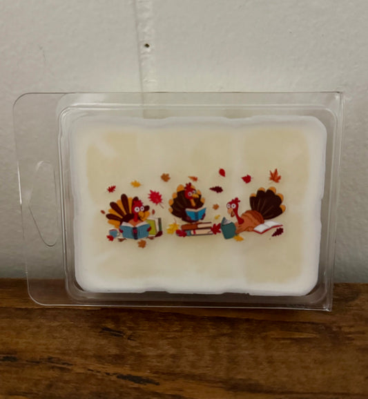 Wax melt with Thanksgiving-themed design of turkeys and leaves in a clear packaging on a wooden surface.