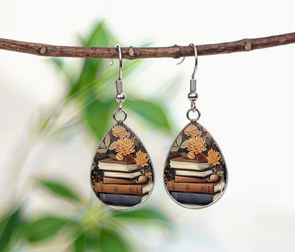 Teardrop glass earrings featuring stacked vintage-style books surrounded by golden flowers and botanical details
