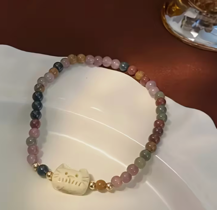 Vintage cat charm bracelet displayed on a dish, showing mixed pastel beads.