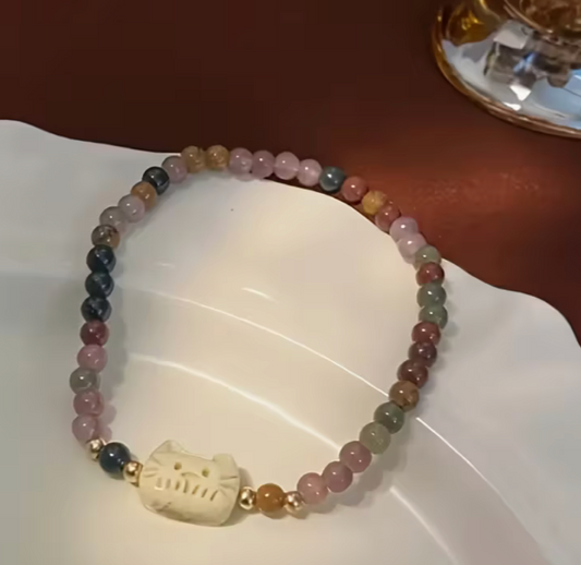 Vintage cat charm bracelet displayed on a dish, showing mixed pastel beads.