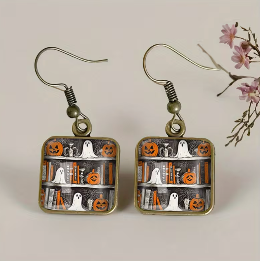Halloween-themed earrings with ghost, pumpkin, and book designs on a neutral background.