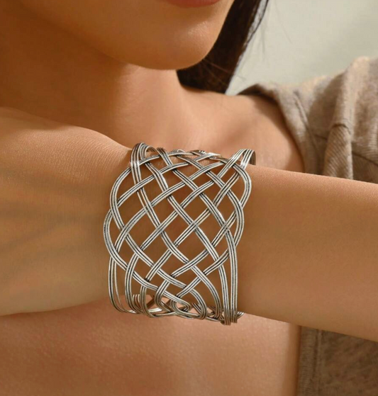 Silver woven cuff bracelet on a person's wrist with a neutral background