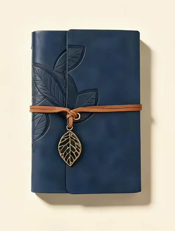 Navy blue pocket journal with embossed leaf design, brown wrap closure and vintage metal leaf charm