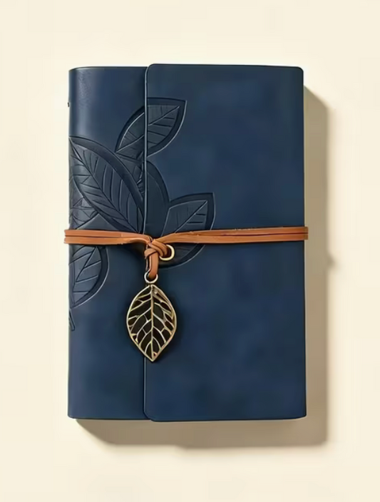 Navy blue pocket journal with embossed leaf design, brown wrap closure and vintage metal leaf charm