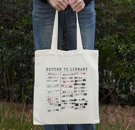 Cream canvas tote bag featuring a vintage library checkout card design inspired by classic library due date cards.