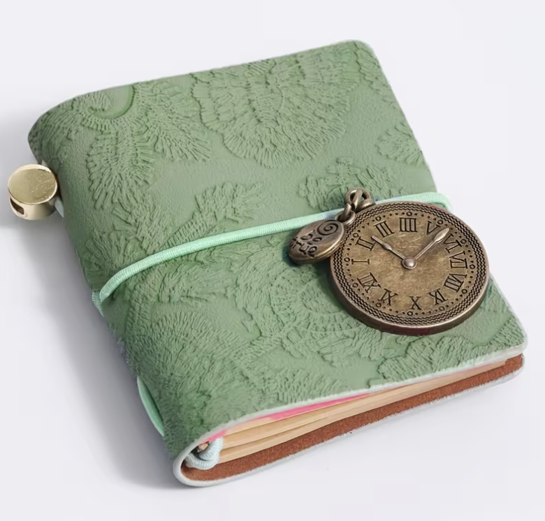 Vintage-inspired mini faux leather notebook with an embossed floral cover, antique metal clock charm, elastic strap closure, and pocket-sized design for journaling and note-taking.