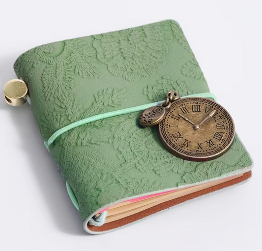 Vintage-inspired mini faux leather notebook with an embossed floral cover, antique metal clock charm, elastic strap closure, and pocket-sized design for journaling and note-taking.