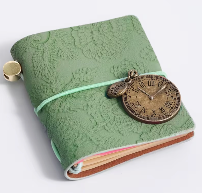 Vintage-inspired mini faux leather notebook with an embossed floral cover, antique metal clock charm, elastic strap closure, and pocket-sized design for journaling and note-taking.