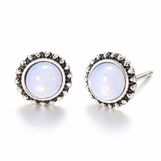 Pair of vintage-inspired white cabochon stud earrings featuring glossy milky white domed centers with a soft opalescent appearance and ornate antique silver-tone sunburst settings on a white background.