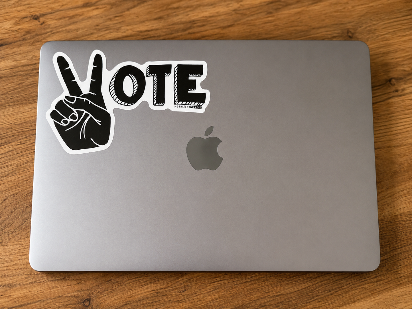 Large black and white Vote vinyl sticker with peace sign hand displayed on a silver laptop.