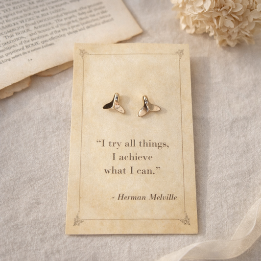 Gold whale tail stud earrings displayed on a vintage style quote card with soft neutral background and floral accents