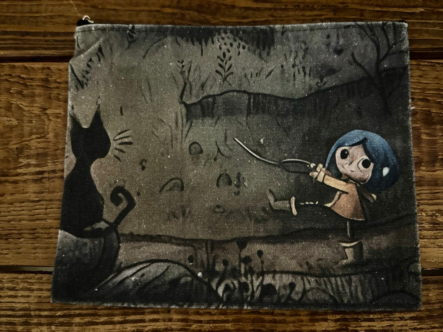 Small pouch with a design of a child holding a sword and a cat in a forest setting on a wooden surface.