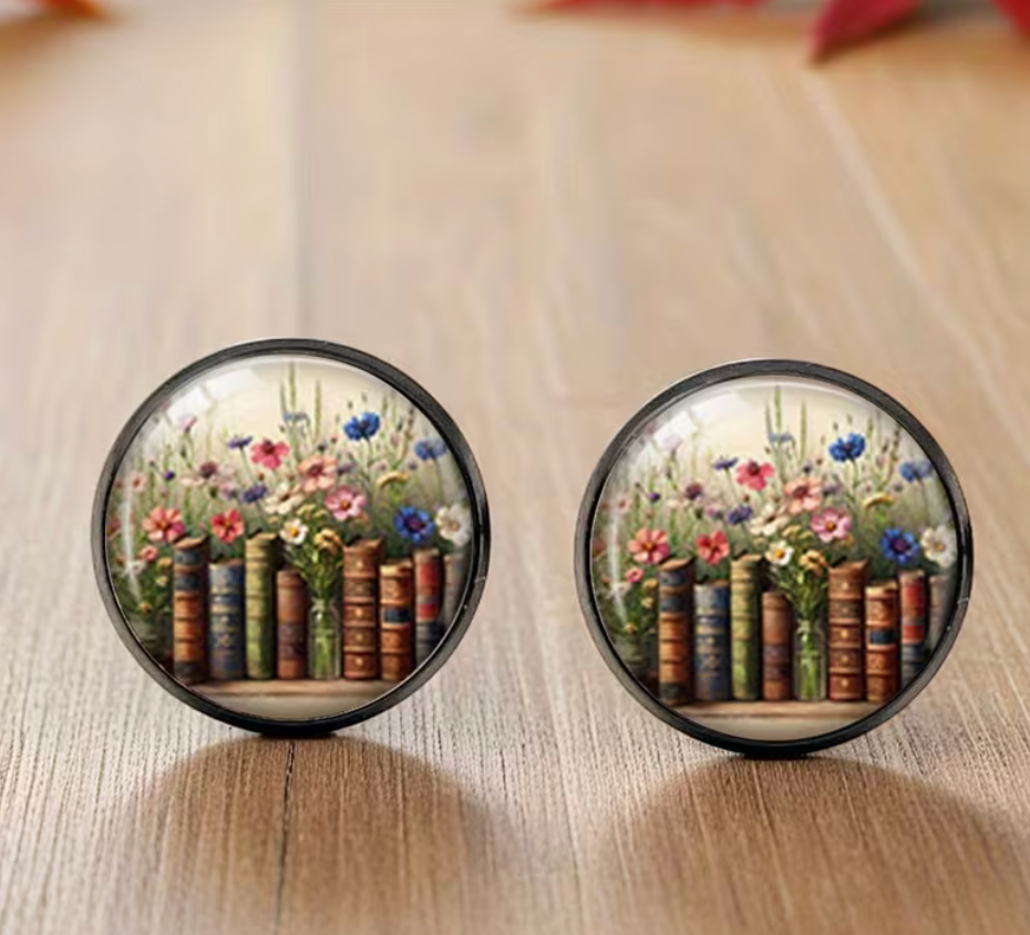 Round glass dome stud earrings featuring colorful wildflowers growing above a row of vintage-style books