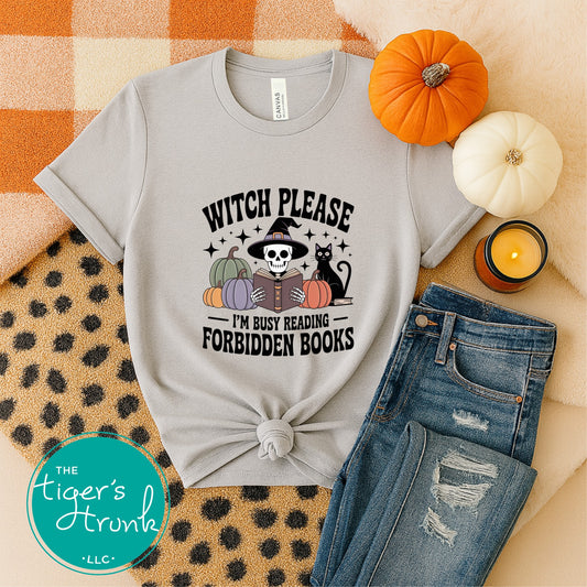 Gray t-shirt with Halloween-themed design, jeans, pumpkins, and candle on a patterned surface.