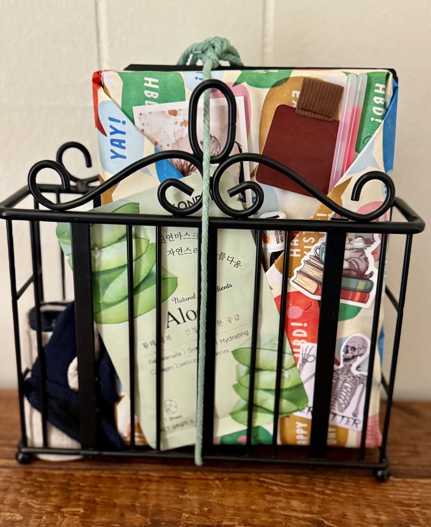 Black metal magazine holder with colorful books and stationery items on a wooden surface.