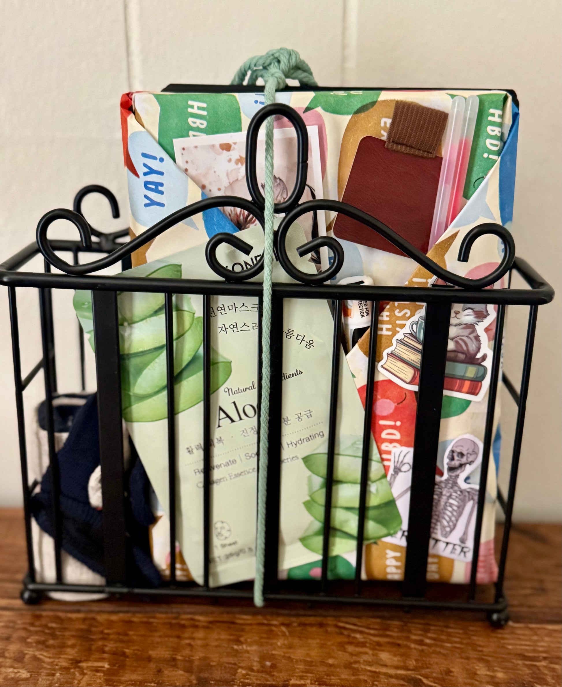 Black metal magazine holder with colorful books and stationery items on a wooden surface.